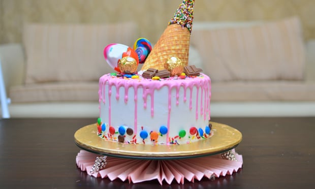 A cute pink birthday cake with an ice cream cone waffle / wafer on top with sprinkles chocolate and lollipop on top for a girl’s birthday