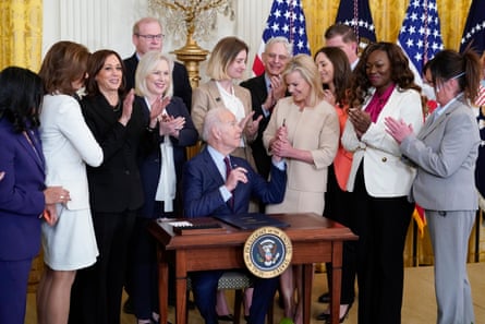 Joe Biden sitting at desk surrounded by applauding women.