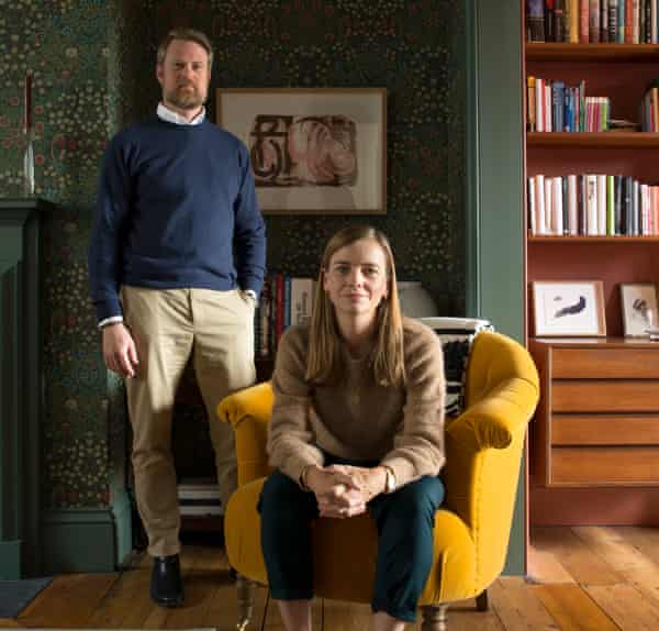 Ed and Alice Workman in their study, Alice in a mustard-colour chair, Ed standing behind