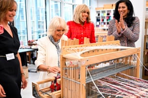 Camilla sits at a weaving machine, watched by a smiling Brigitte Macron and Leena Nair