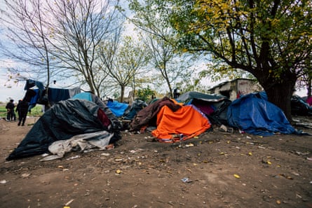 A group of flimsy tents on muddy ground under a tree, with washing hung on a line