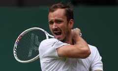 Daniil Medvedev is photographed with his mouth open as if he is yelling something; in this head and shoulders picture his right arm is bent so he holds his racket round his neck and over his left shoulder. He wears a white top and is thin and wiry with light brown hair that is receding at the temples.