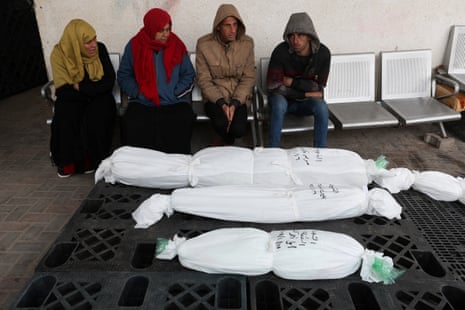 People sit on 17 January in Rafah with the bodies of Palestinians who were killed in an Israeli strike.