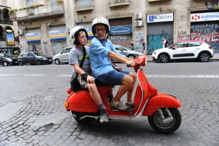 A man and a boy on a red Vespa on a street