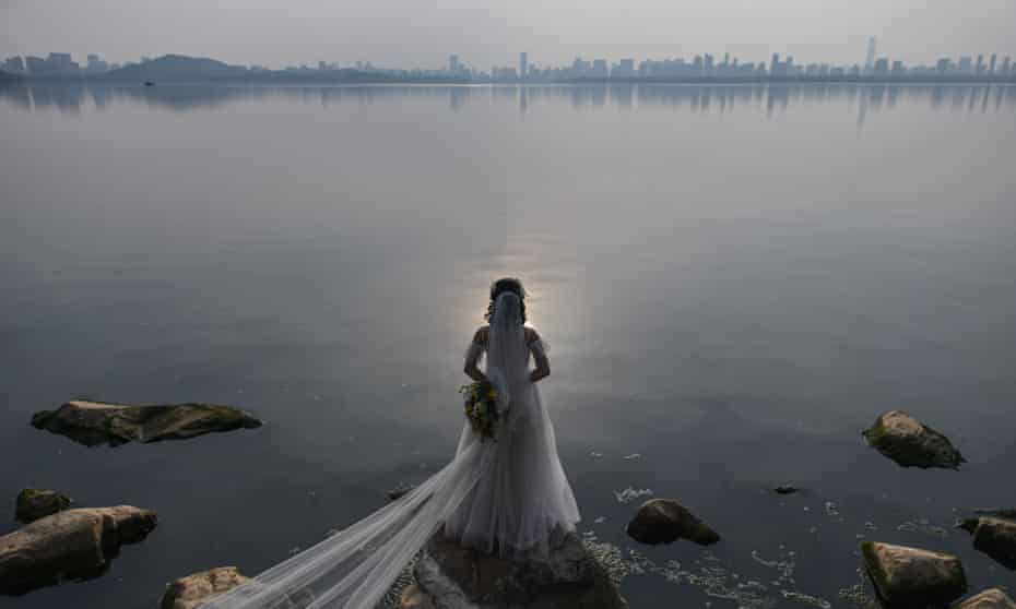 A bride, poses for a wedding photographer next to East Lake in Wuhan