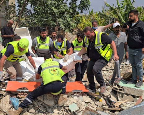 Half a dozen rescue workers carry a body wrapped in a white sheet.