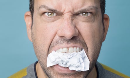 A close-up of Michael Spicer's angry face with a piece of screwed-up paper between his teeth