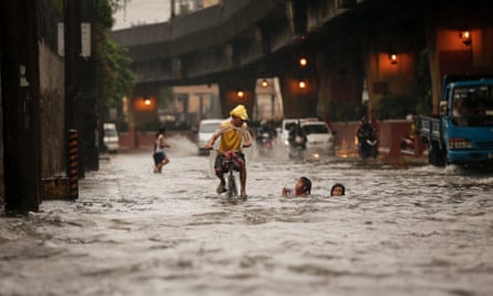 A Filipino on a bike passes children in a flooded street in Manila, the Philippines, in 2016.
