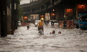 A Filipino on a bike passes by children frolicking along a flooded street. Heavy monsoon rains have resulted in floods across Manila
