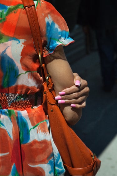 Manhattan, 2010- a tightly cropped view of a women in a bright red and blue floral dress seen from behind. her hand and dramatically varnished nails visible