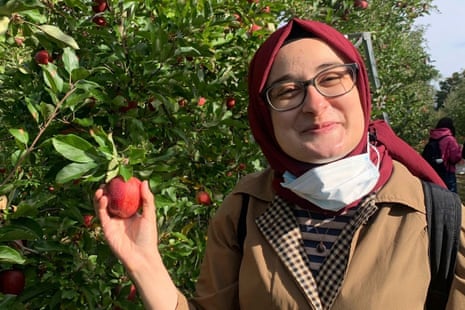 Rumeysa Ozturk in an apple orchard smiling as. she holds an apple.