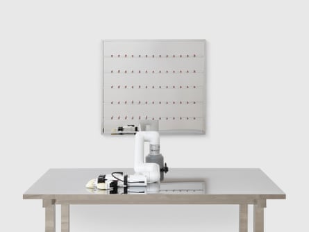 A robotic arm sits motionless on a table, a display of pills on a board hangs on the wall behind