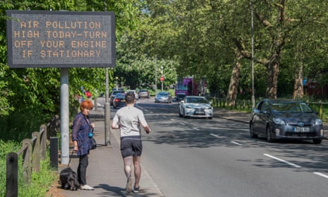 A woman waits to cross the road with her dog as joggers are not daunted by the Air pollution warnings on a busy road