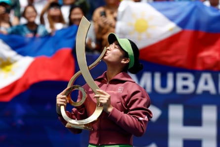 Alexandra Eala celebrates with the DC Open trophy as fans fly the Filipino flag behind her.