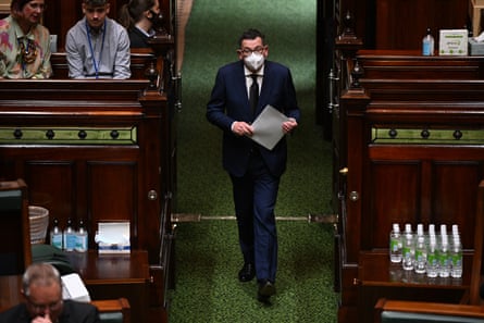 Dan Andrews in mask carrying paper walking between parliamentary benches