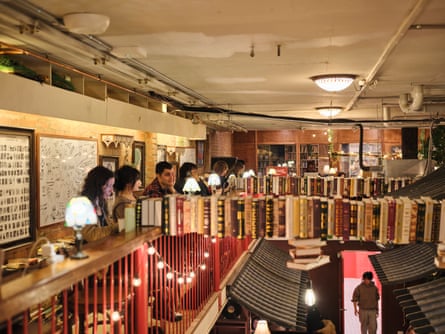 Students seated at tables near a bannister. A ‘chain’ of books floats suspended from the bannister to a faux Japanese temple-esque roof