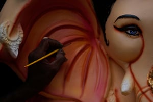 A close-up of the artist’s hand holding a paintbrush as they paint the elephant head of Ganesha