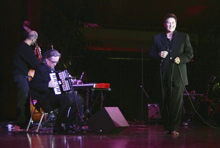 Kd lang smiles on stage while a seated accordionist and a bassist play
