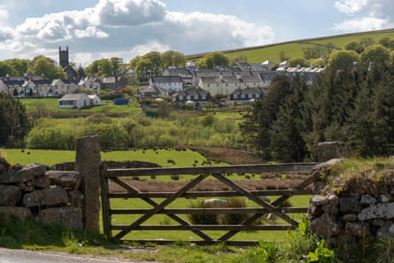 A country gate and fields in the foreground with a village and church tower in the background