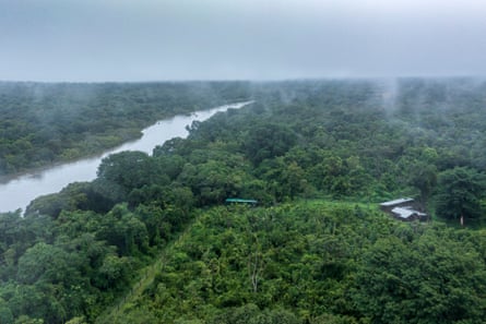An aerial view of a tree-filled landscape with a river and a small cluster of buildings
