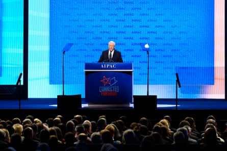 a man in suit speaks on stage into microphone