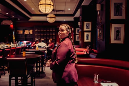 woman in burgundy jacket looks to the side as she stands inside a restaurant