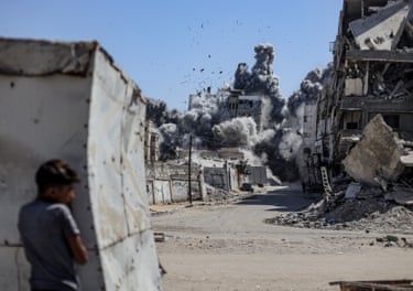A boy watches from behind a truck as thick smoke rises from a building hit by a missile