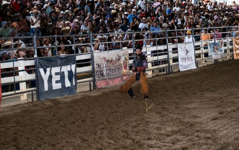 A cowboy stands at the edge of an arena as the crowd cheers him on from the stands