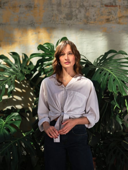 Gretta Ray, wearing a white shirt, standing in front of a leafy green plant
