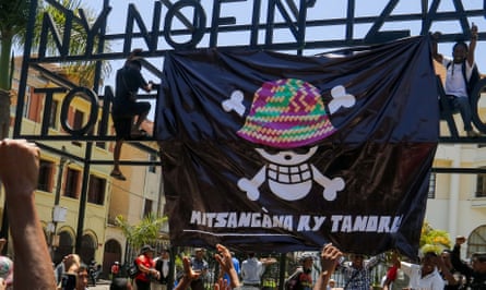 Protesters hang a banner featuring a Japanese manga-style skull and crossbones with a hat