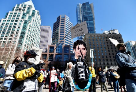 A group of people hold signs reading messages such as ‘No jobs on a dead planet’ at a protest in front of city buildings
