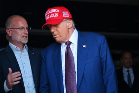 Two men speak with each other, the elderly one with a Maga hat on