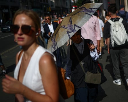 People endure a heatwave on Oxford Street in the UK on Tuesday. One woman holds an umbrella.