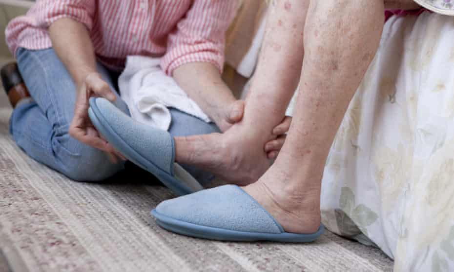 Younger carer helping old person put on slippers