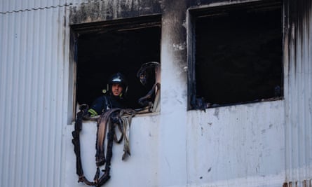 A firefighter looks out of a blackened, fire-damaged window