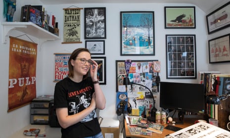 Anna Readman standing in a studio  filled with framed prints and memorabilia, wearing a Love & Rockets T-shirt