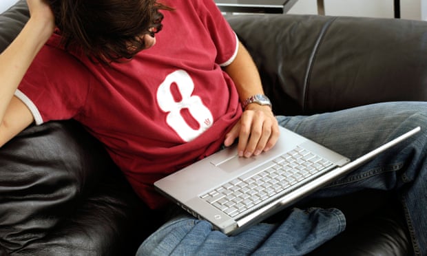 Man wearing red t-shirt and jeans sitting on sofa using laptop