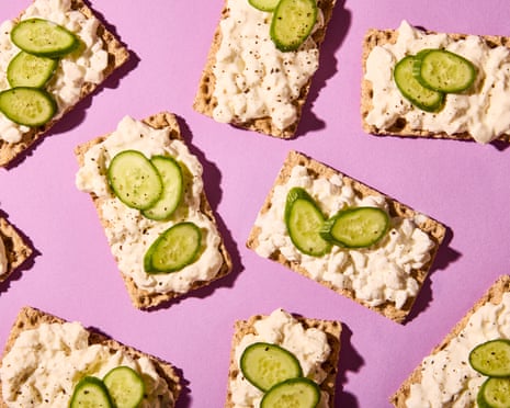 Crackers topped with cottage cheese and cucumber slices arranged on a pink surface