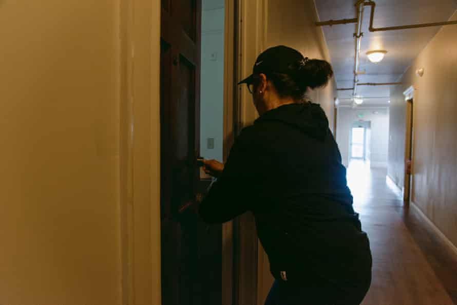 A woman stands in the hallway of an apartment building, opening the door to her home.