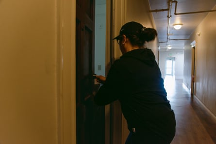 A woman stands in the hallway of an apartment building, opening the door to her home.