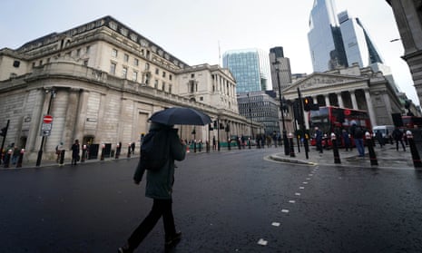 A person with a black umbrella walks past the Bank of England in the city of London