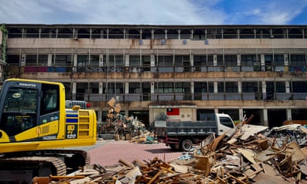 An abandoned building against the backdrop of a blue sky with a yellow construction vehicle in front of it.
