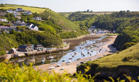 A sea inlet at the bottom of a green steep-sided valley with sand and water at the bottom and boats moored.