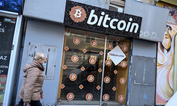 A woman walking past a small shopfront with a big bitcoin sign above the door