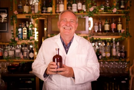 Prof David Nutt in a lab coat in front of a bar or lab, holding a bottle of Sentia.