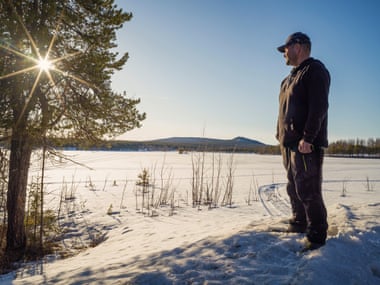 Kuhmunen stands on frozen lake with hills in distance