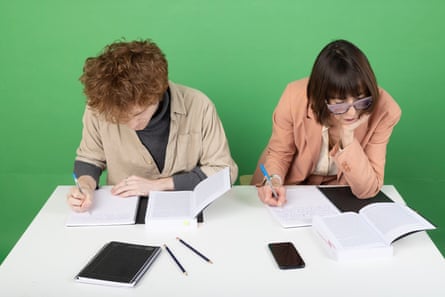 The pair concentrate on their writing seated at desk, side-by-side