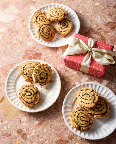 Gurdeep Loyal’s poppy seed XO pinwheels look like swiss rolls but beige. A small, red gift box tied with a golden bow sits among the snacks.