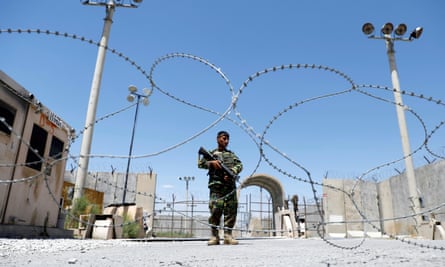 A soldier alone standing guard, framed by coils of razor wire and floodlight towers against a blue sky
