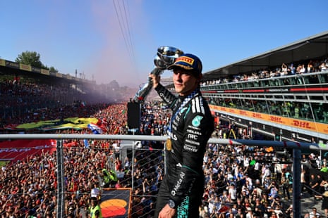 Fans cheer Kimi Antonelli as he raises his trophy above his head on the podium